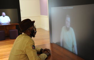 African American man in hat listening to a video essay in Words Matter gallery