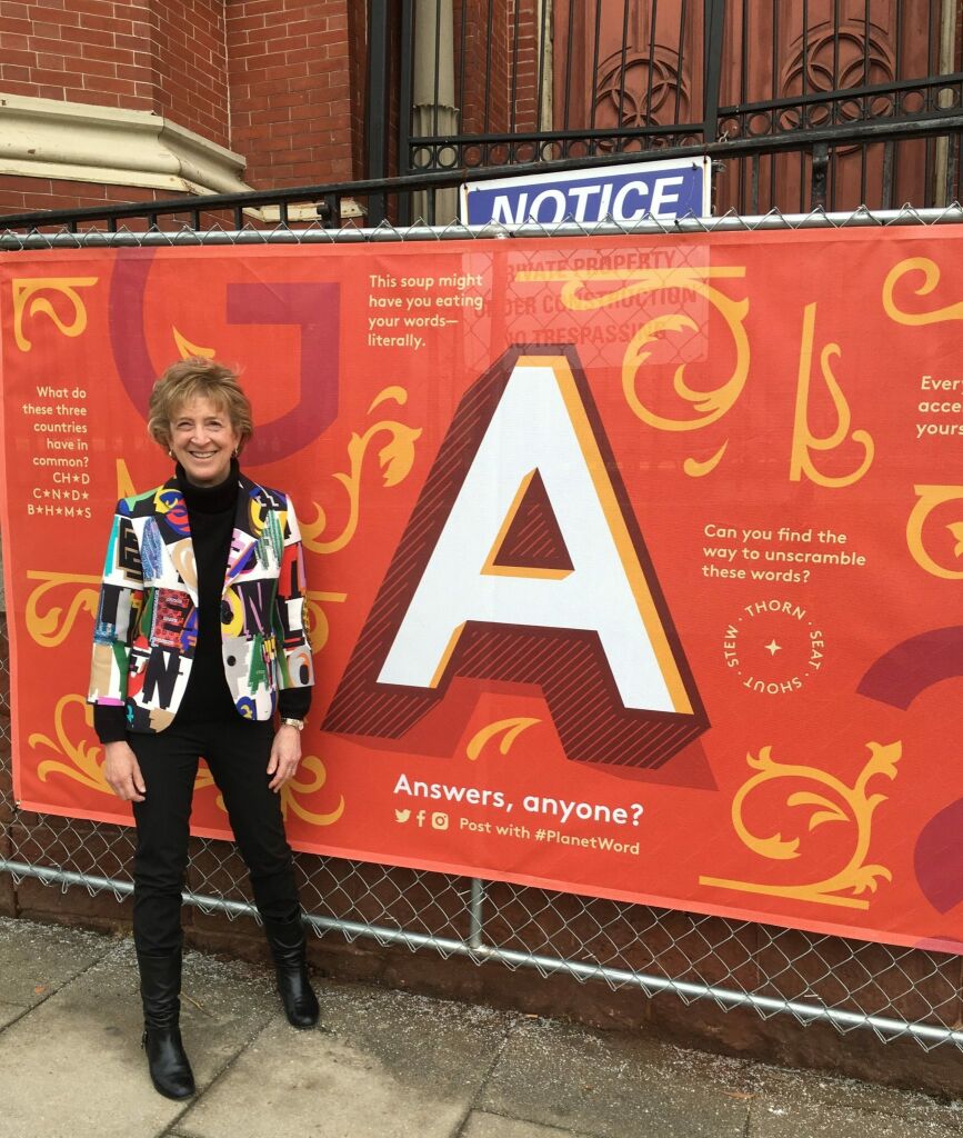 Ann Friedman standing in front of a construction fence at Planet Word decorated with a large letter A and riddles